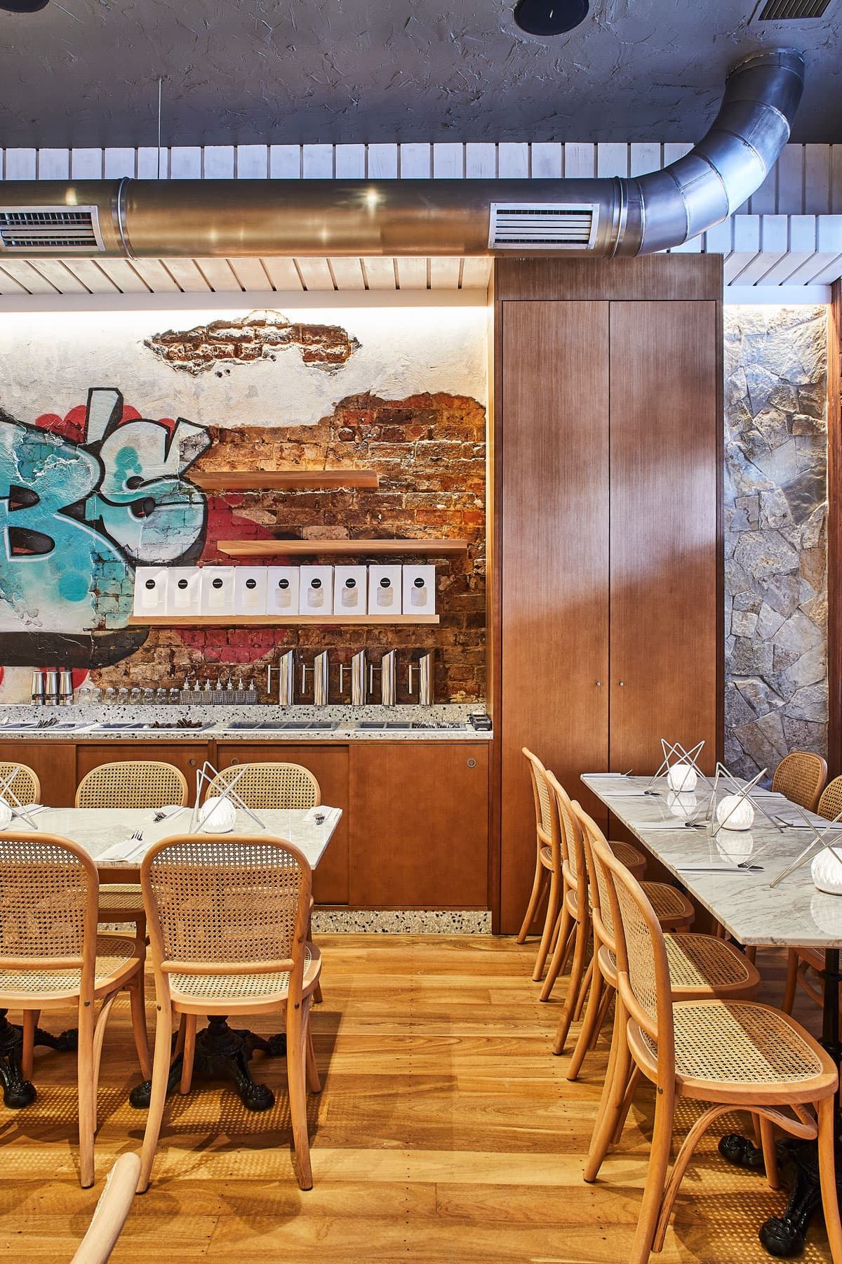 Interior seating area at Frankie B's Food House Parramatta featuring a section of wall with artistic graffiti, exposed brick, and shelves with decor items.