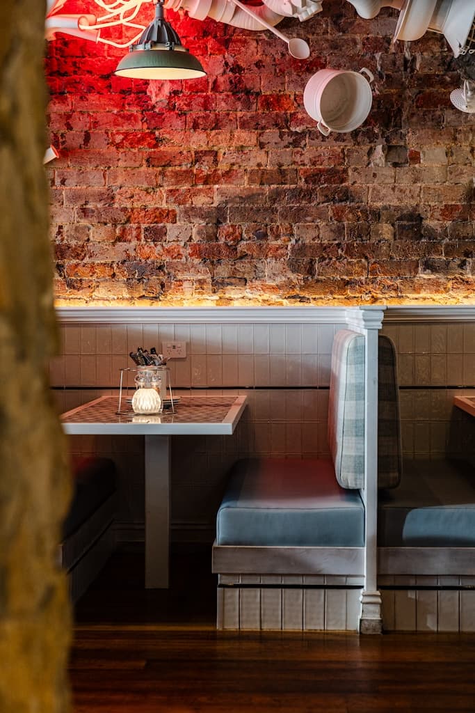 Intimate booth seating with a mosaic tabletop at Frankie B's Food House Parramatta, featuring a rustic brick wall and soft lighting.