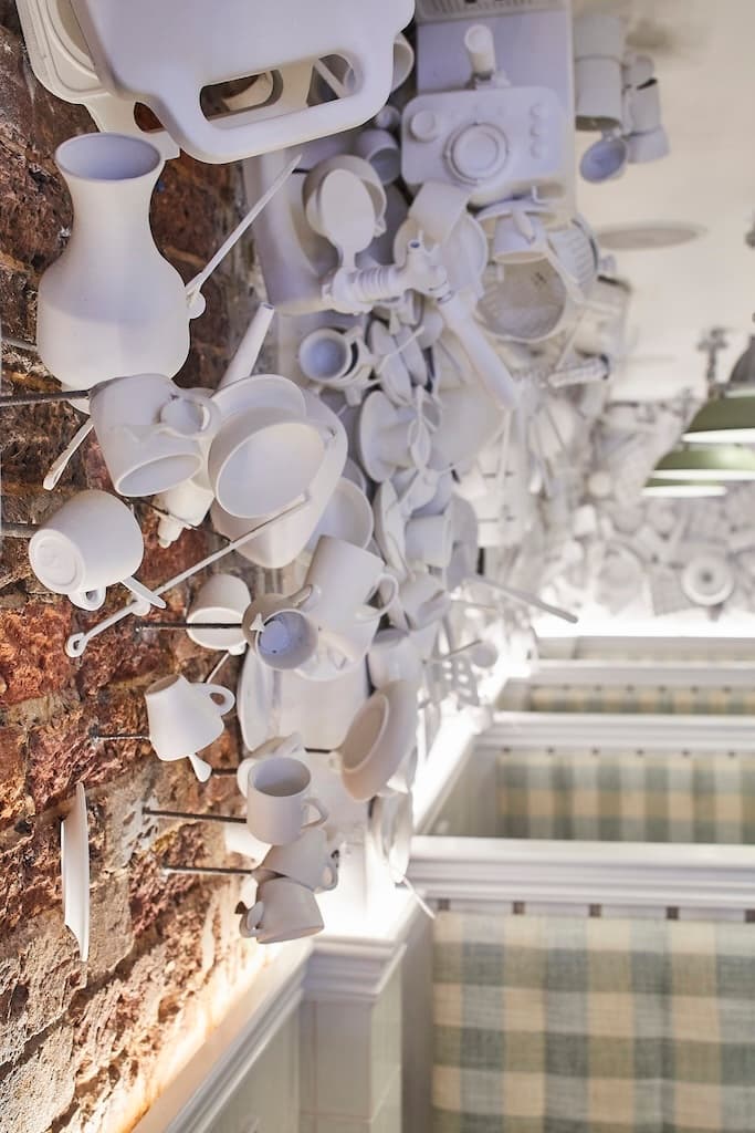 Close-up of a wall display featuring an arrangement of white kitchen utensils, including cups, pitchers, and plates, mounted against an exposed brick background at Frankie B's Food House Parramatta.